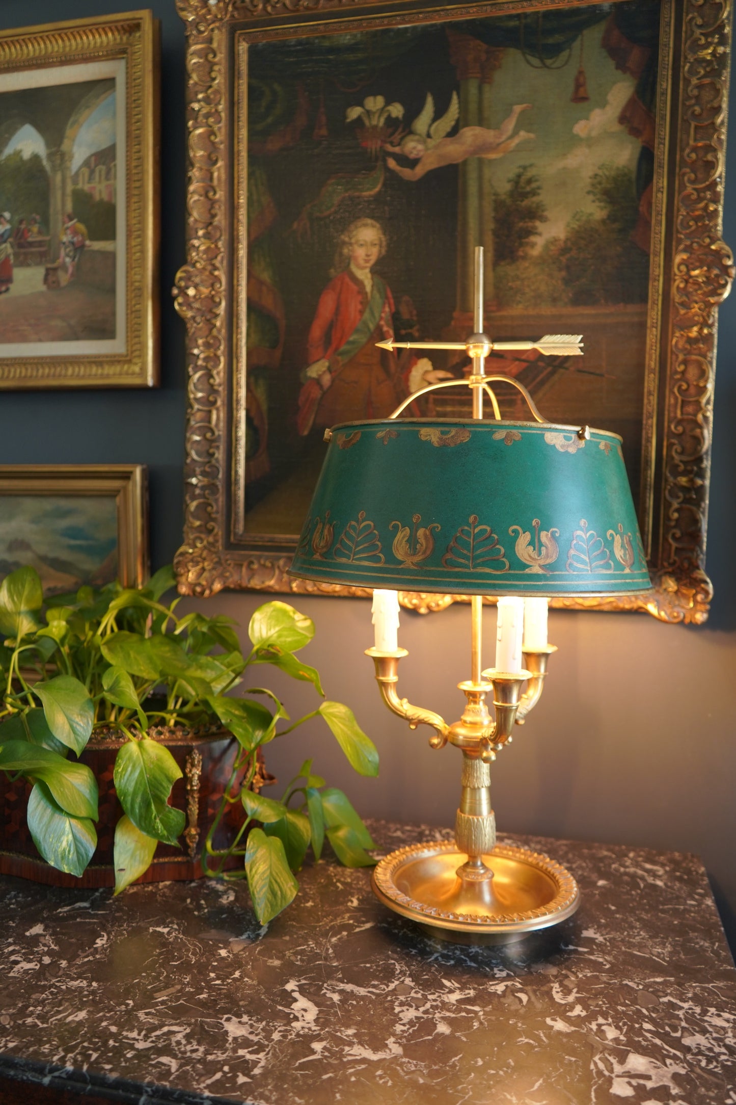 Decorative lamp with a green shade on a marble surface, framed paintings in the background.