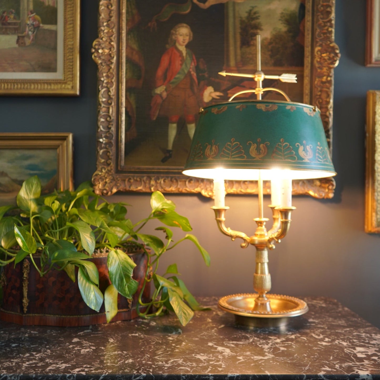 Vintage-style lamp with decorative shade on a marble surface, framed paintings in the background.