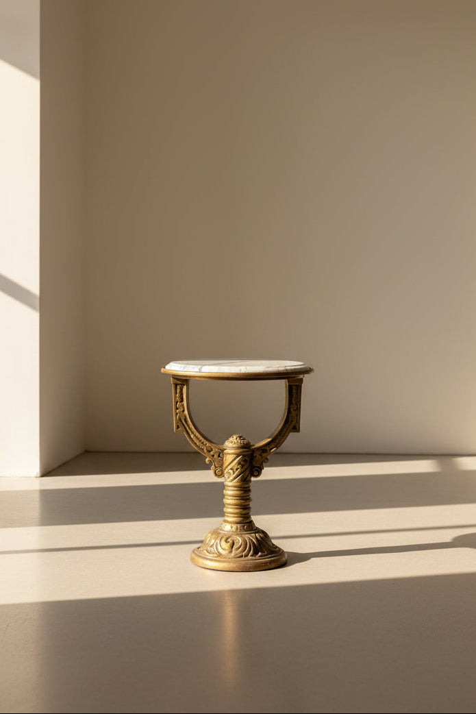 Small round table with marble top and gold decorative base on a dark floor.