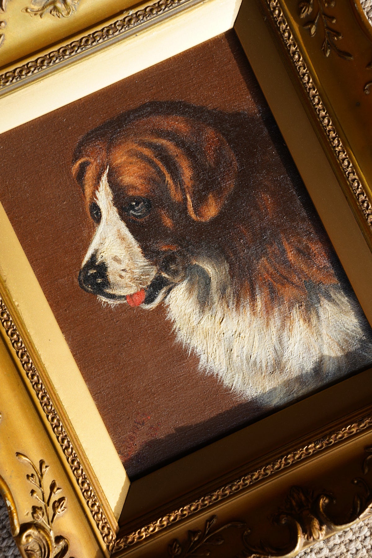 A framed oil painting of a brown and white dog looking upward, set in an ornate gold frame.