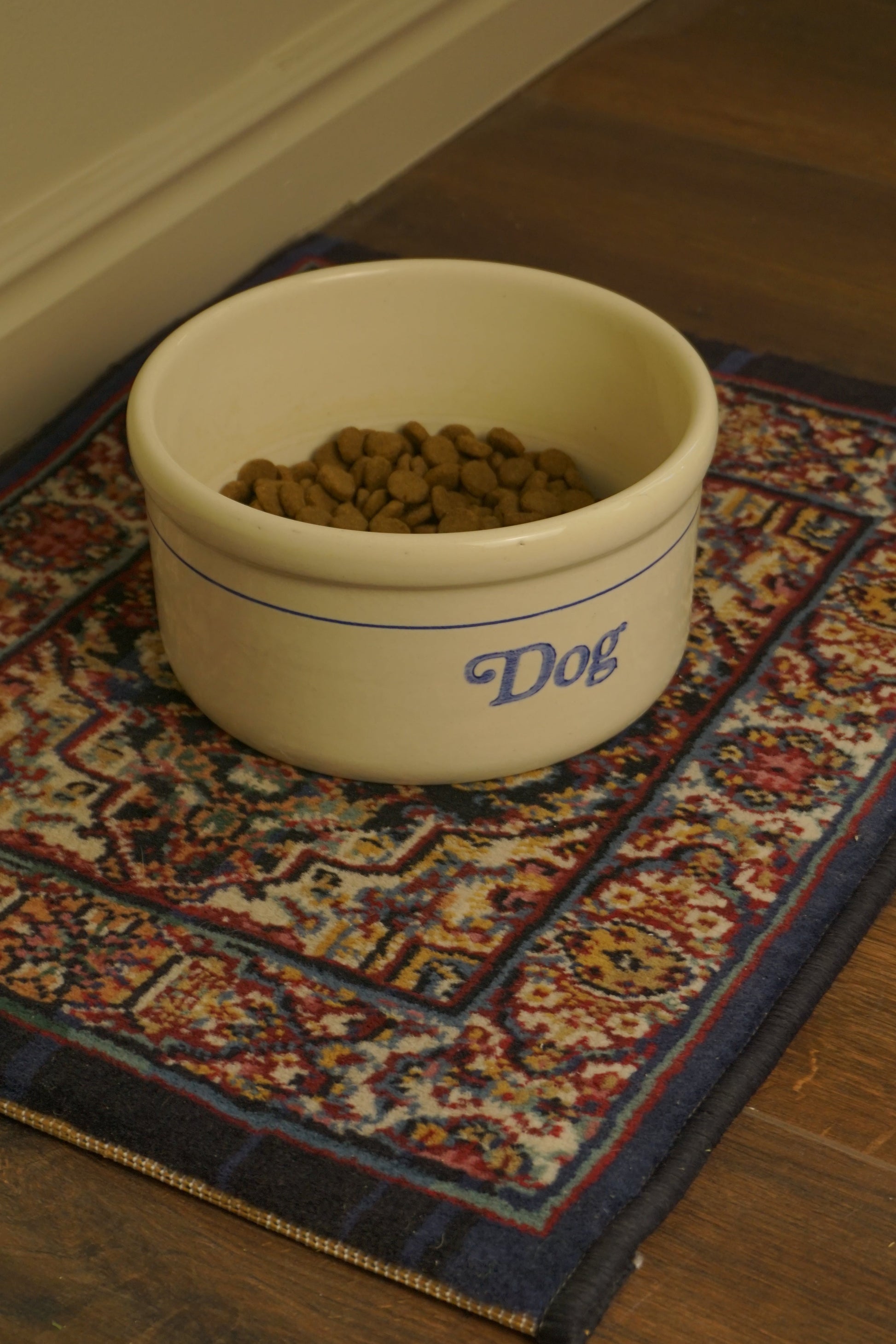 Dog food bowl on small Persian style rug used as a pet mat

Navy and red mini rug styled under a ceramic dog bowl

Close view of rug border under pet dish
